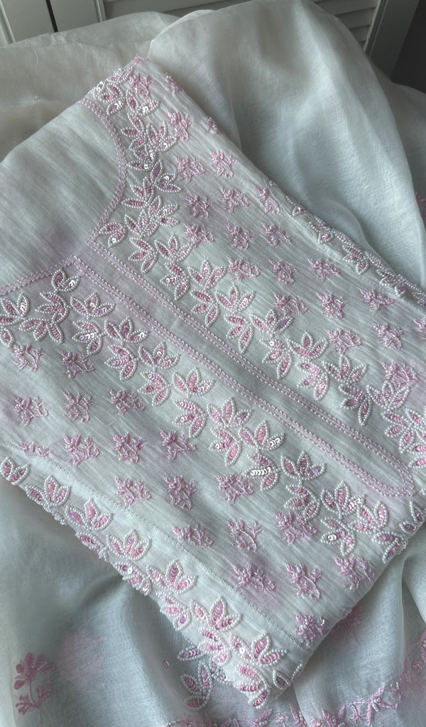 A white Mul Chanderi semi-stitched kurta and dupatta set with pink floral chikankari work, lying on a white fabric.